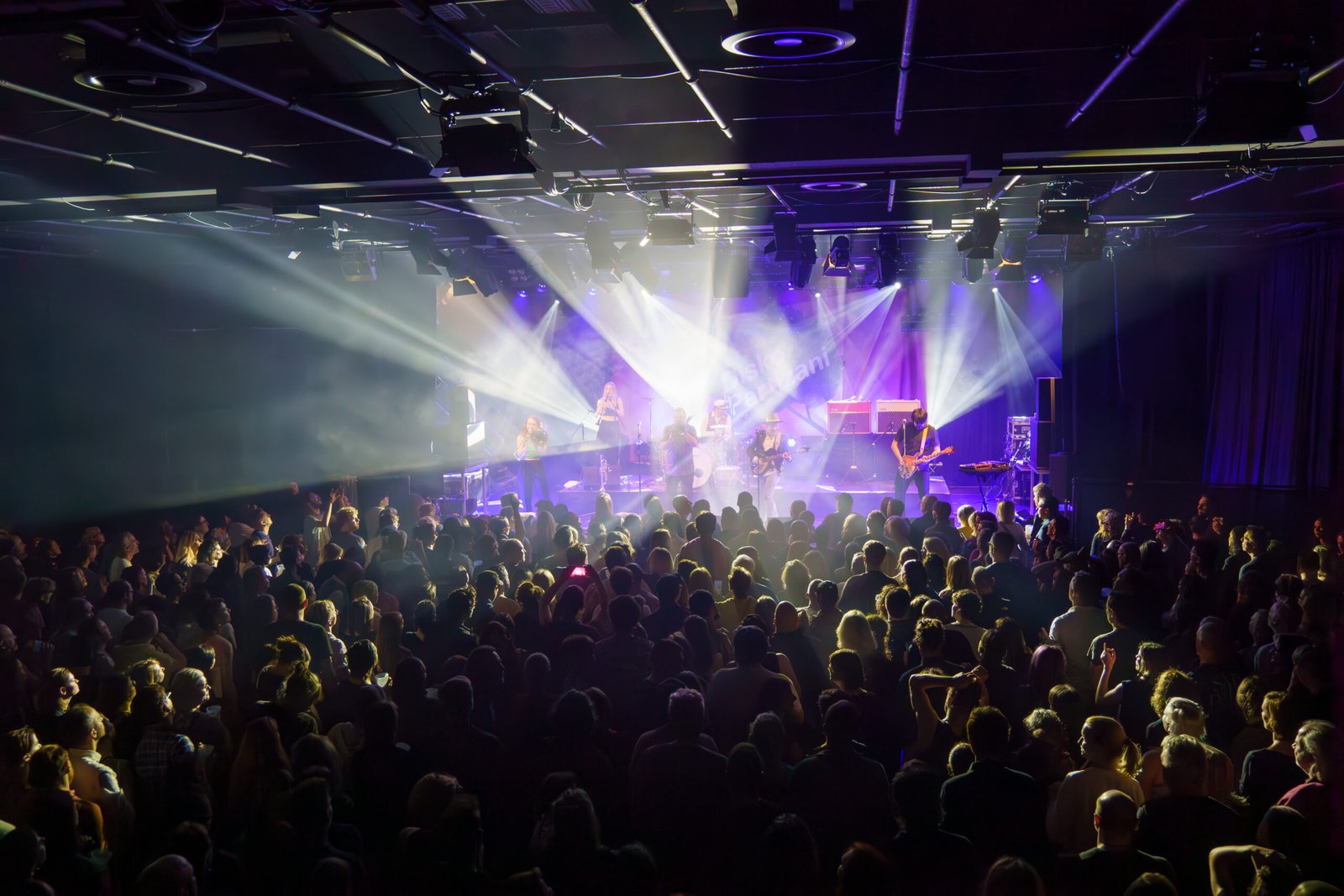 Concert crowd facing a stage lit with white and purple beams