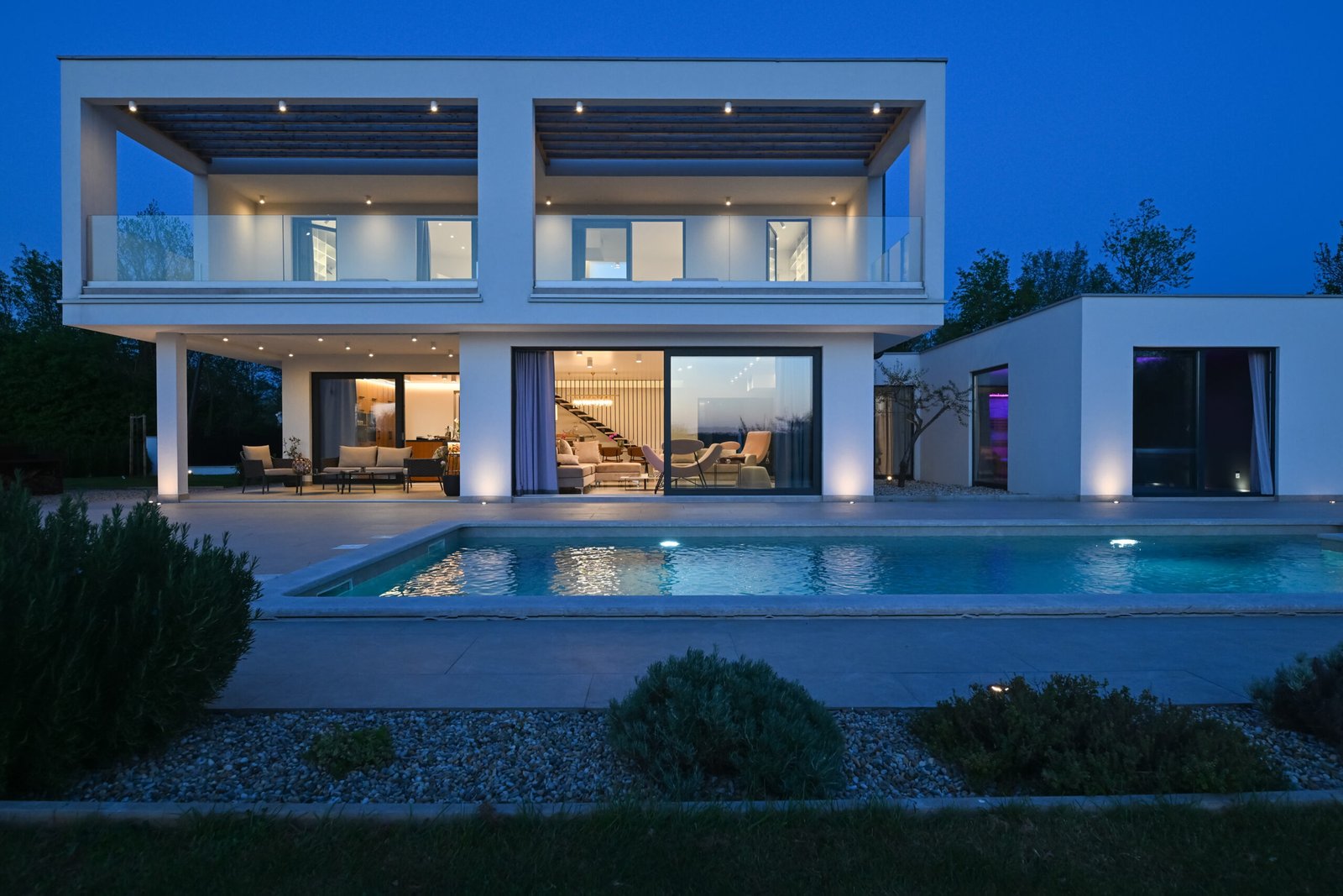 Modern flat-roof PARTAS prefab villa at dusk with lit interiors and a pool in front