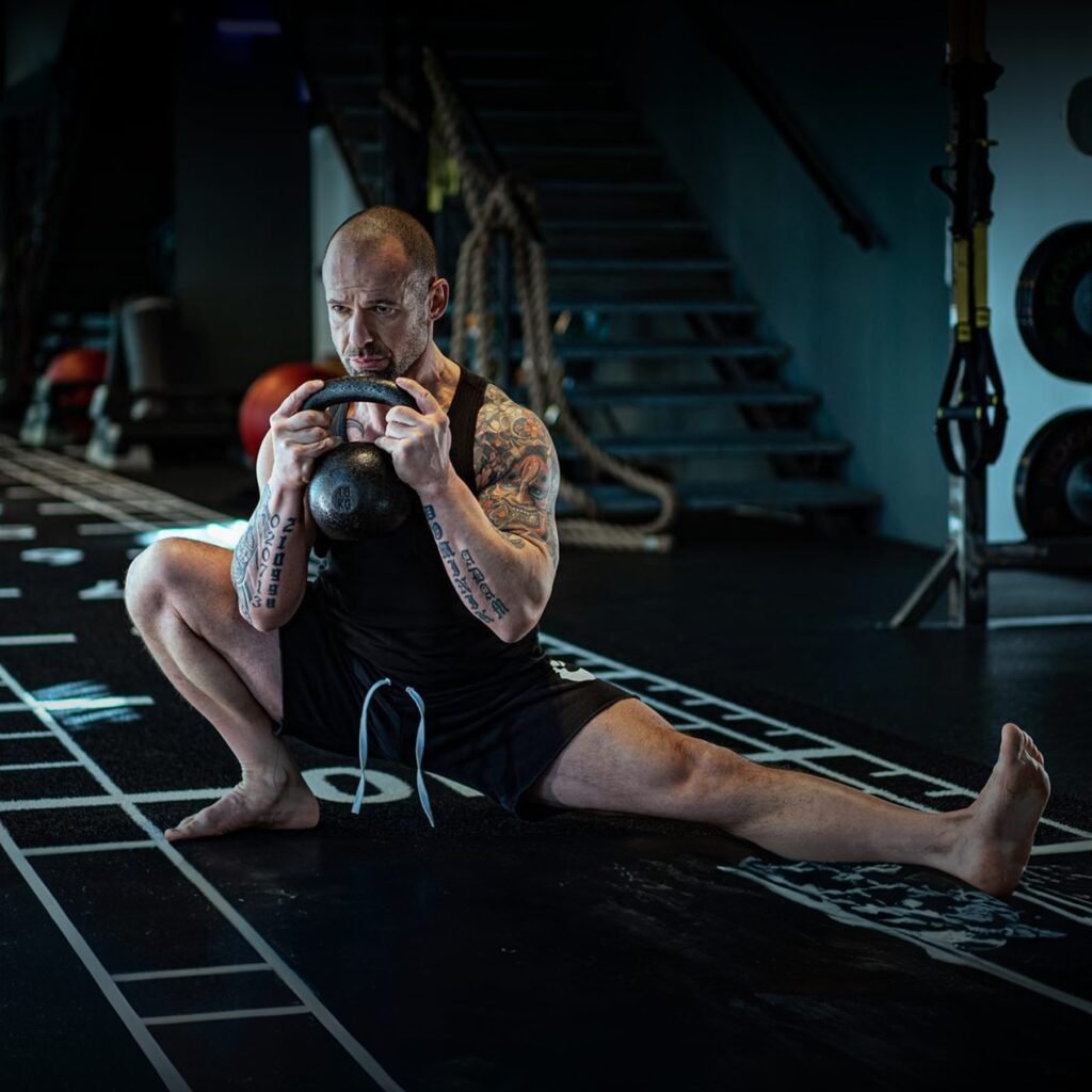 DNT coach Dalibor Nikolic in a deep split squat holding a kettlebell in a dark gym